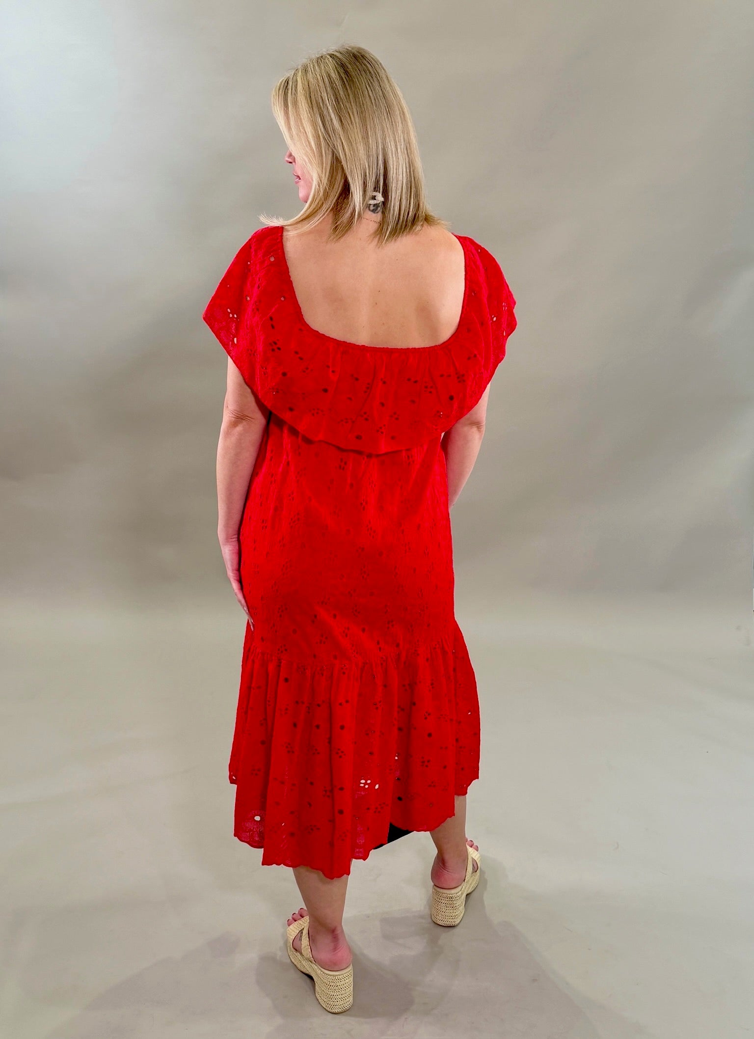 Rear view of a woman wearing a red eyelet dress against a plain background