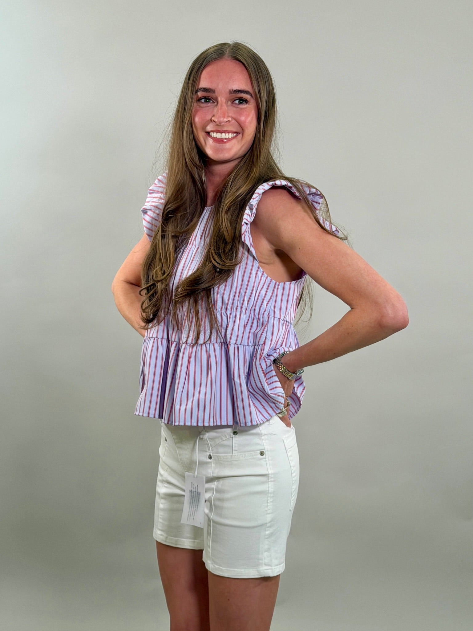 Side view of a woman wearing a striped top and white shorts against a plain background