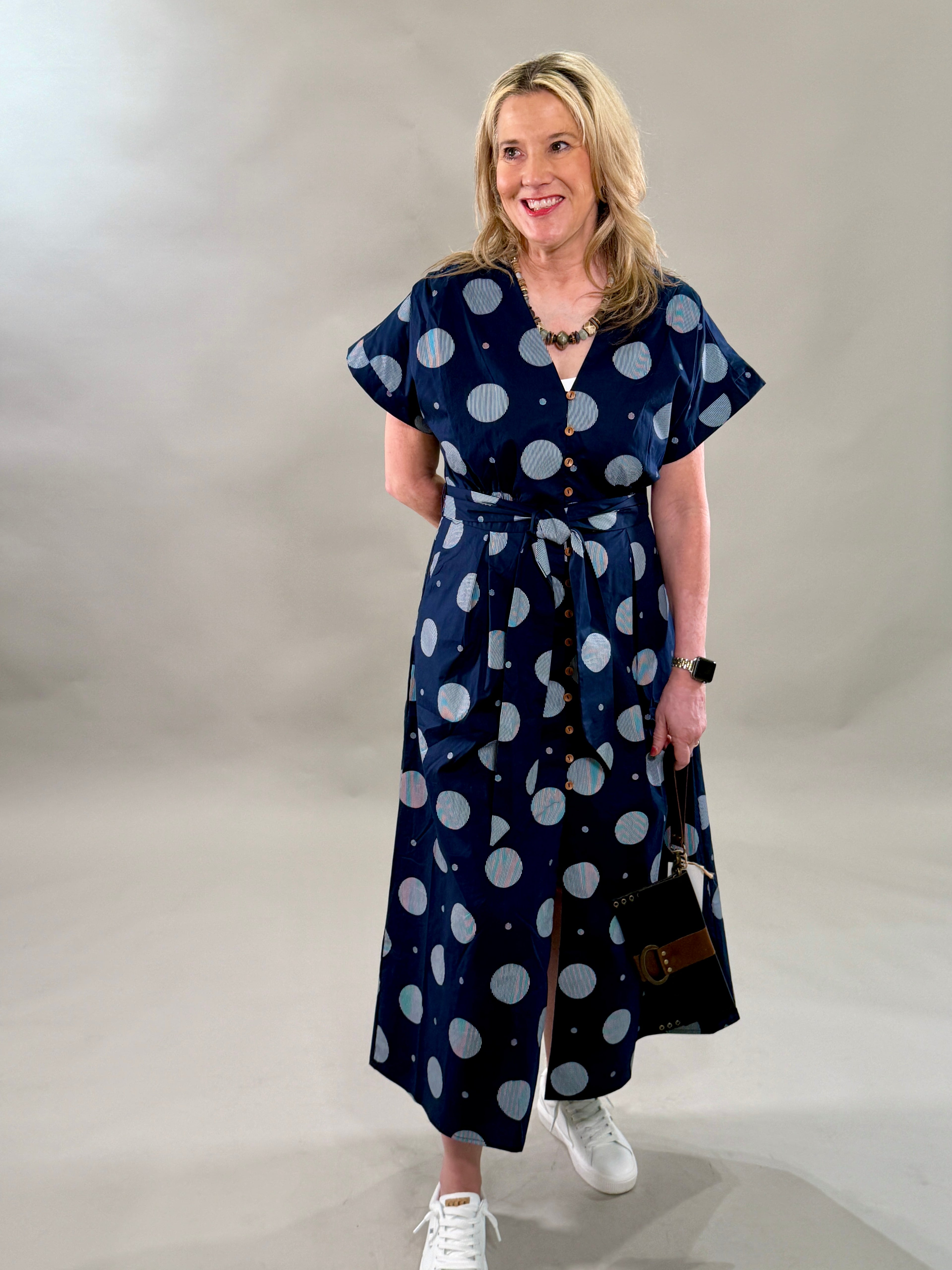 Woman wearing a navy dress with white polka dots against a plain background