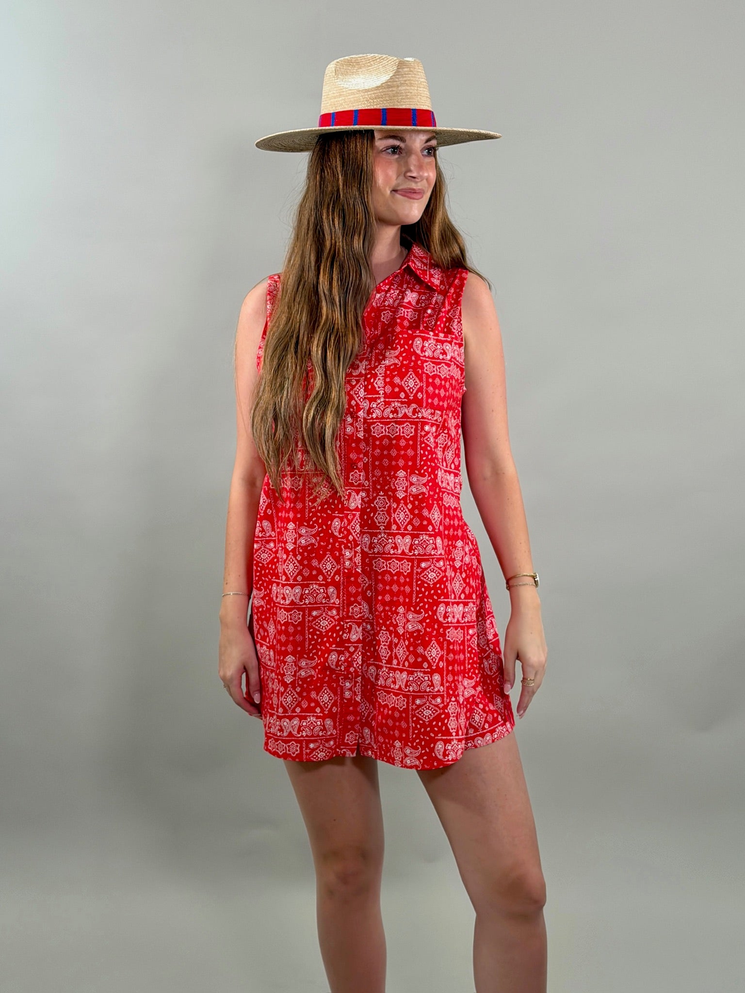 Woman wearing a red patterned romper and straw hat on a gray background
