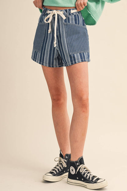Person wearing blue and white striped shorts with a green sweater and black sneakers on a beige background