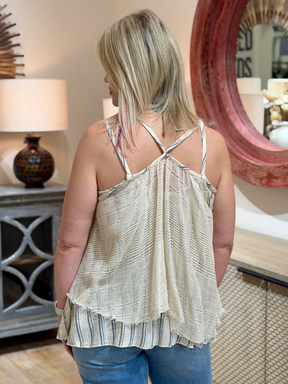 Close up rear view of a woman wearing a cream and grey textured striped cami tank top with blue jeans.