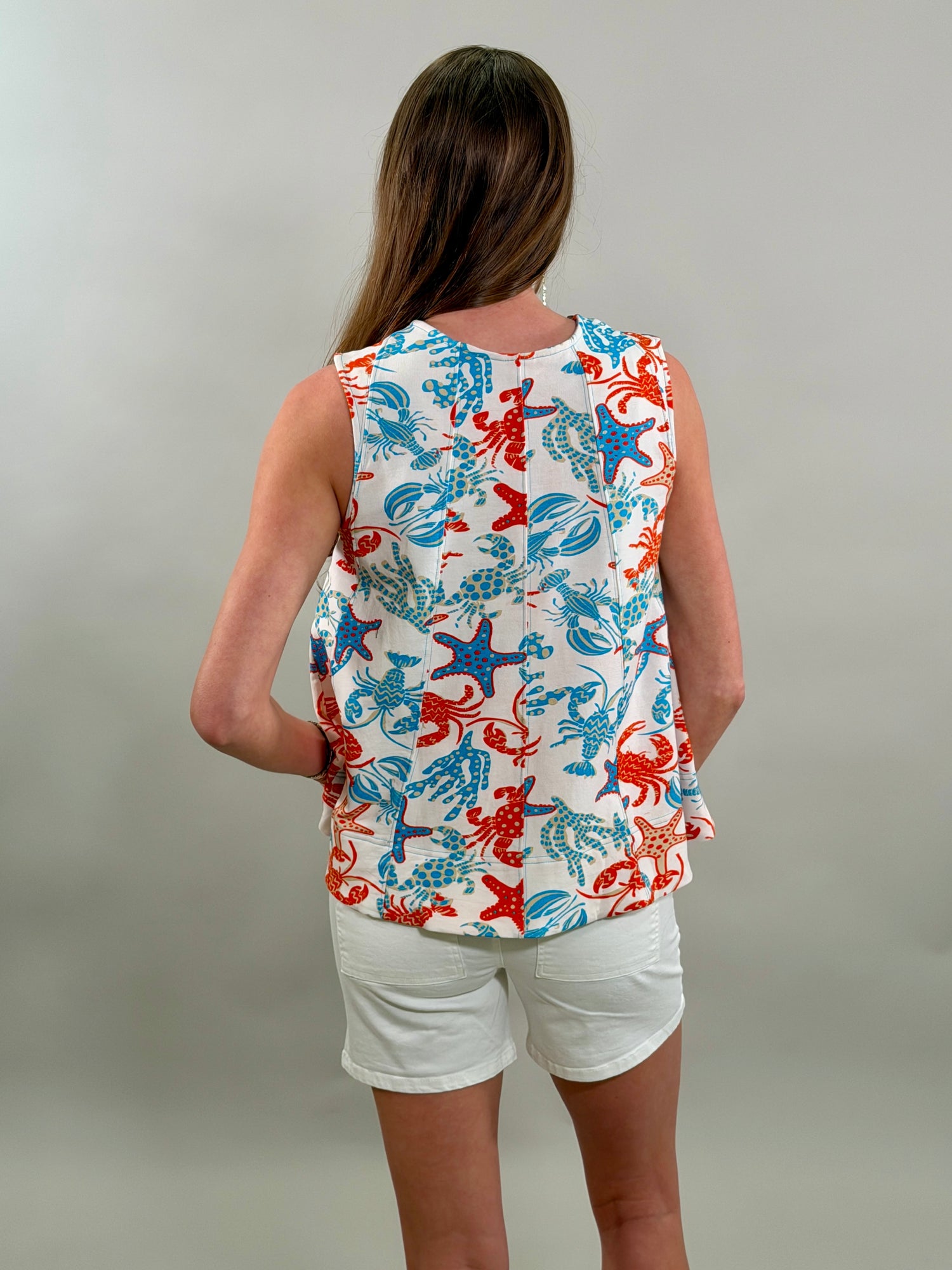 Person wearing a sleeveless top with a colorful crab pattern on a plain background