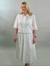 A smiling blonde woman wearing a white geometric eyelet cropped button-up shirt with a matching maxi skirt.