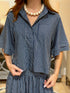 A woman wearing a navy blue and white vertically striped short-sleeve collared shirt with matching striped skirt, styled with a chunky white beaded necklace.