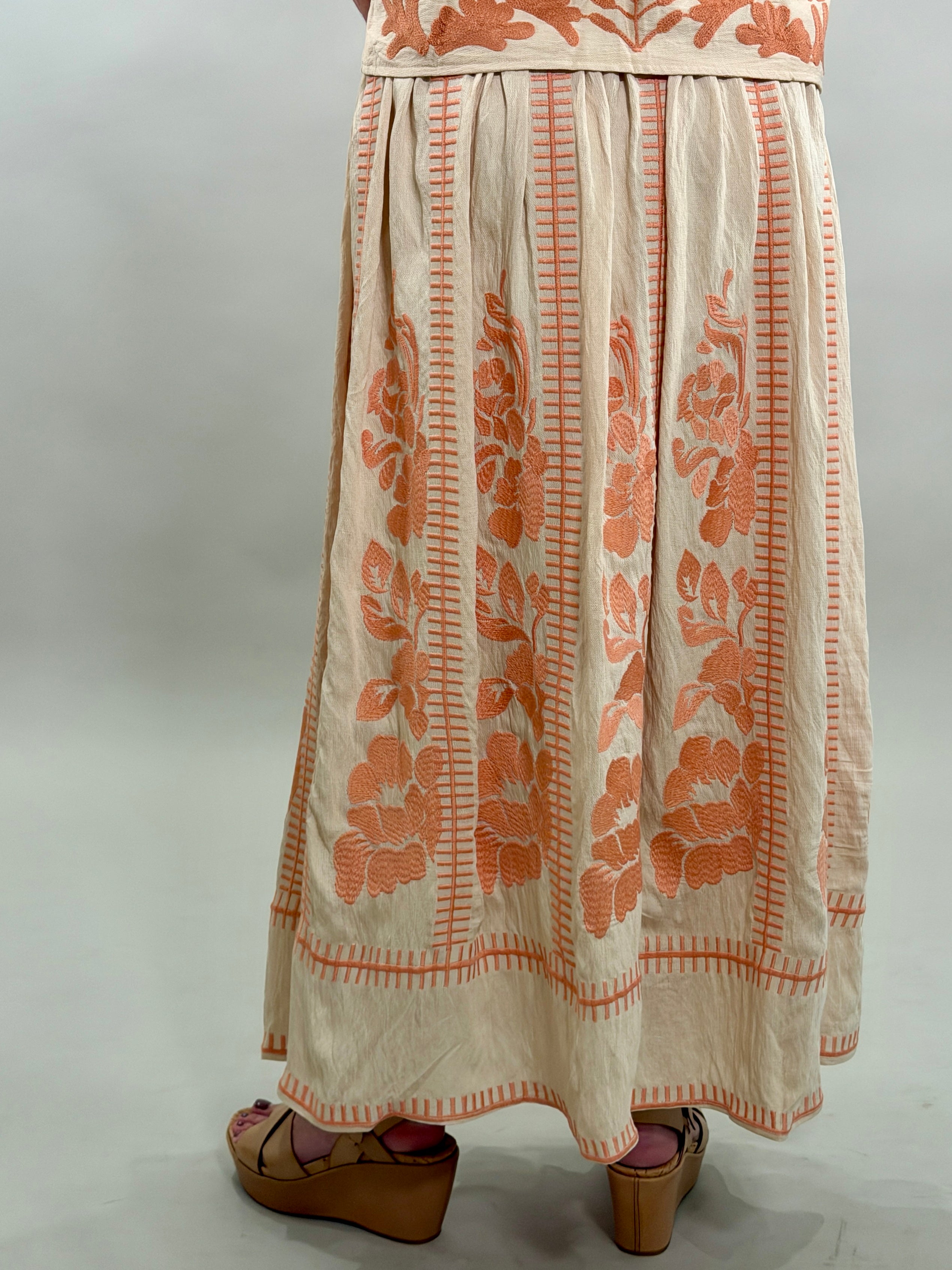 Rear view of a long embroidered skirt with coral patterns on a plain background