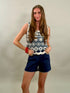 Woman wearing a sleeveless top with white floral patterns and navy shorts on a plain background