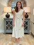 A young woman with reddish hair smiling while wearing an elegant cream cotton midi dress with vertical crochet insets and a matching waist tie.