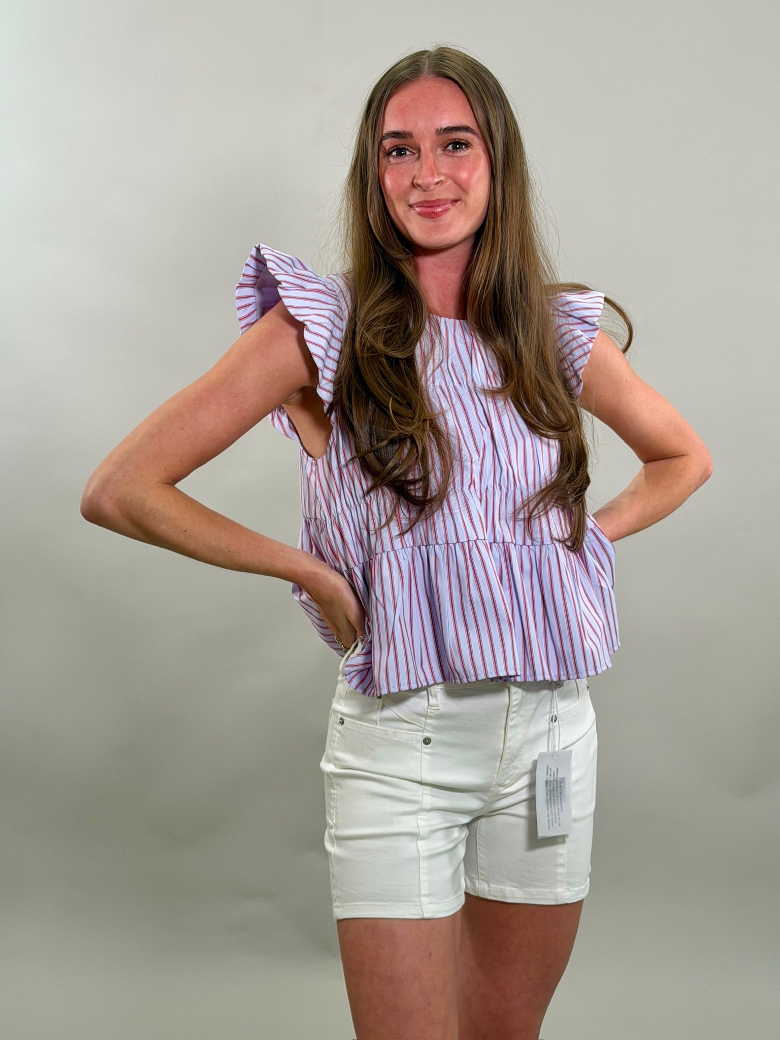 Woman wearing a blue, red and white striped top and white shorts against a plain background