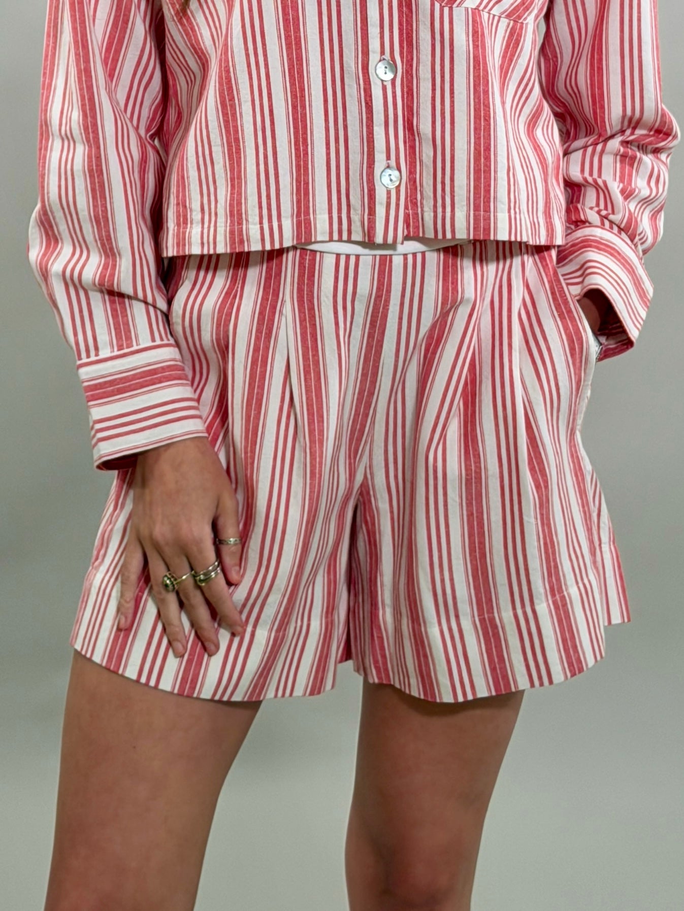 Close-up of a woman wearing tailored red and white striped shorts with front pleats and a matching cropped long-sleeve button-down shirt.