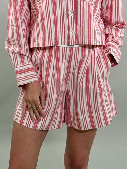 Close-up of a woman wearing tailored red and white striped shorts with front pleats and a matching cropped long-sleeve button-down shirt.