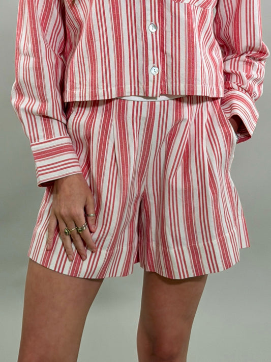 Close-up of a woman wearing tailored red and white striped shorts with front pleats and a matching cropped long-sleeve button-down shirt.