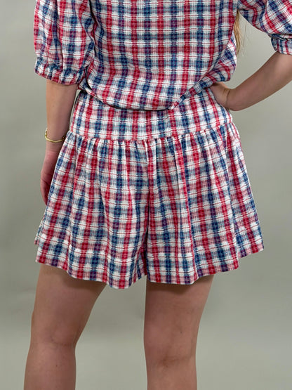Person wearing a red, white, and blue plaid outfit on a plain background