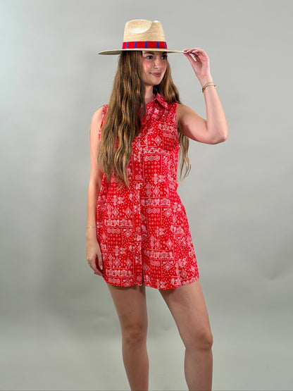 Woman wearing a red patterned romper and straw hat on a gray background
