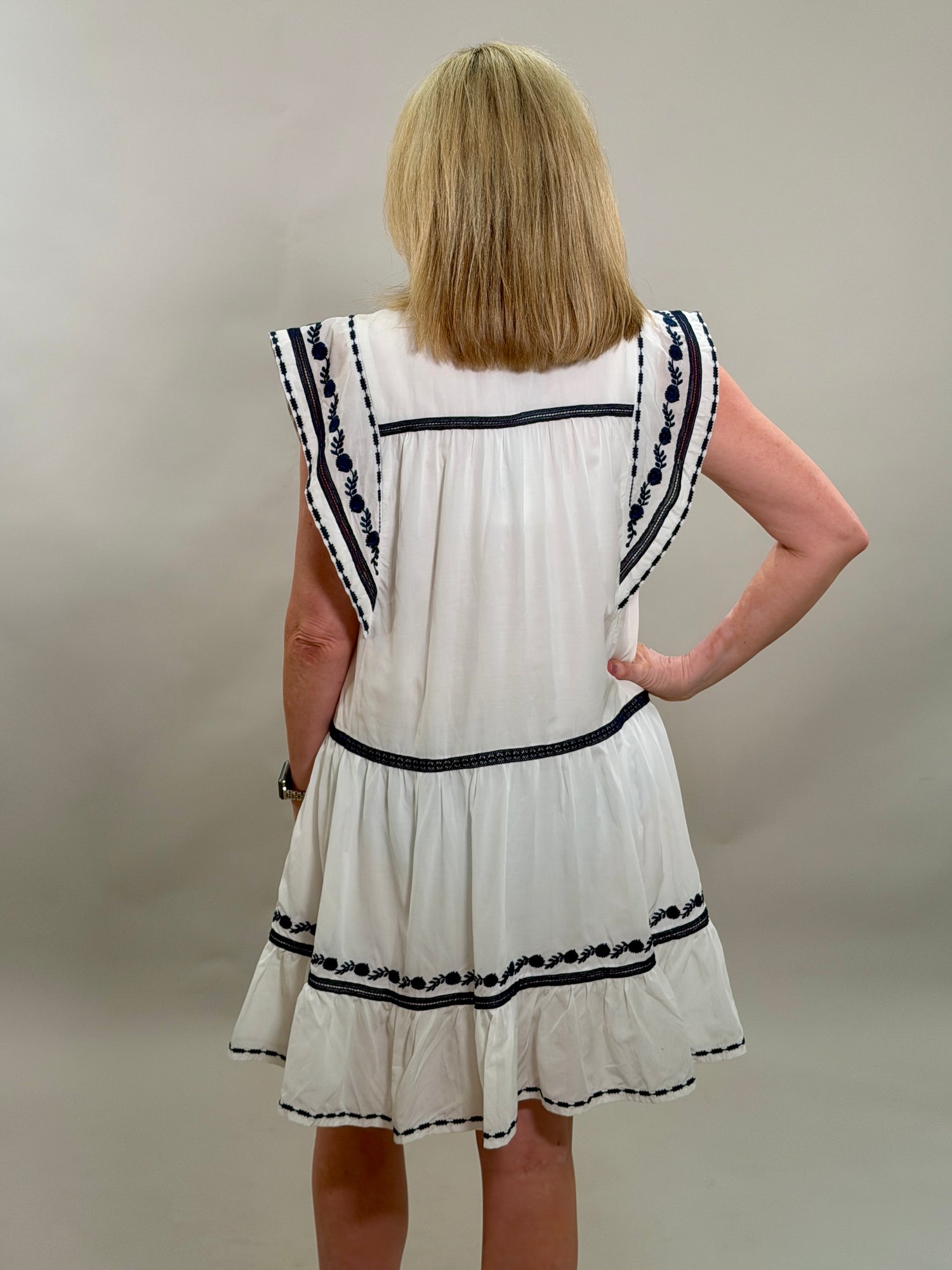 Woman wearing a white dress with navy trim against a plain background