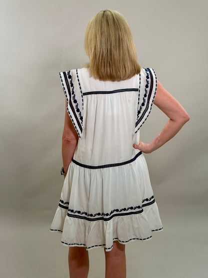 Woman wearing a white dress with navy trim against a plain background