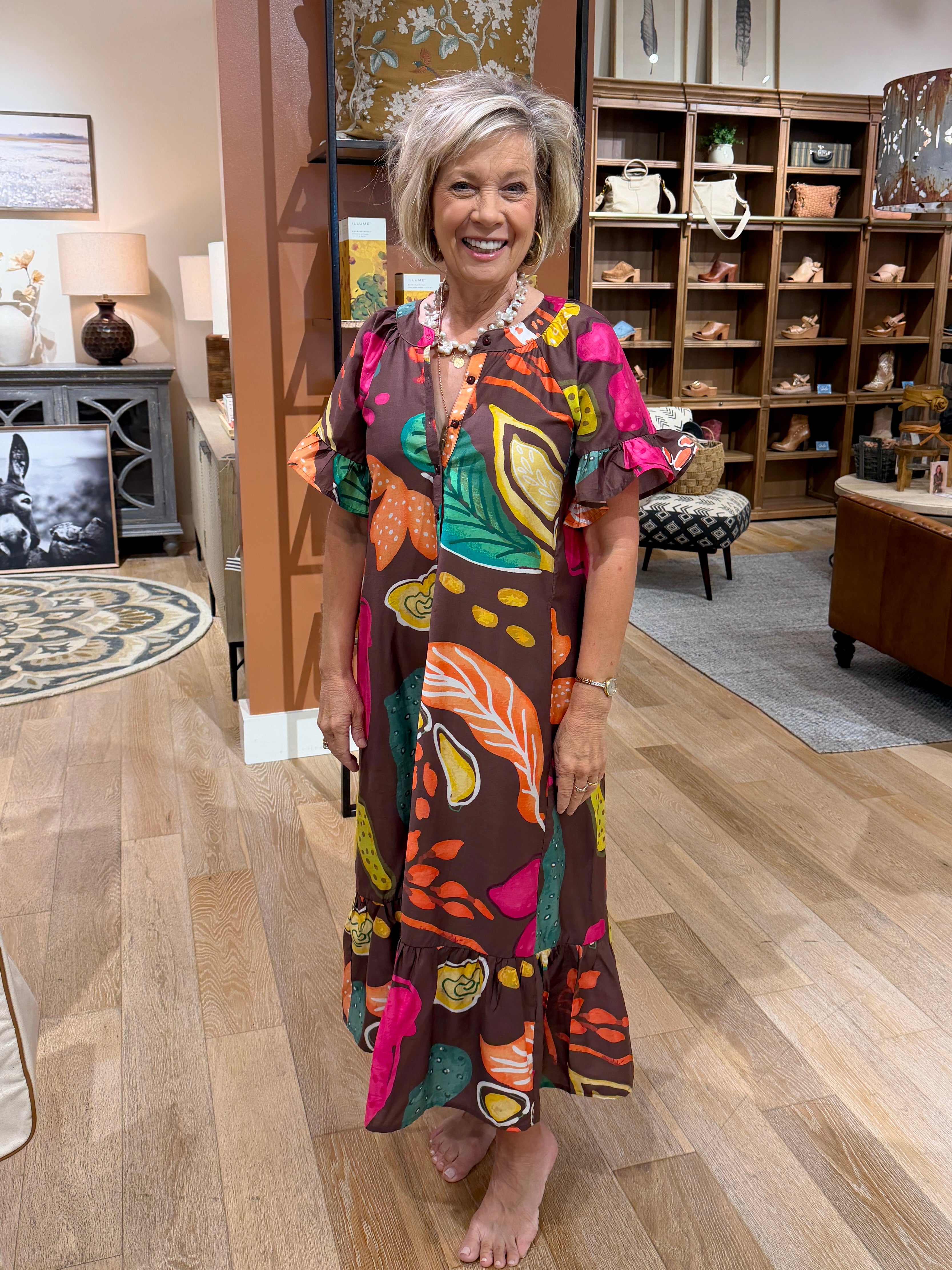 Woman wearing a brown midi dress with colorful tropical leaf prints and flutter sleeves.