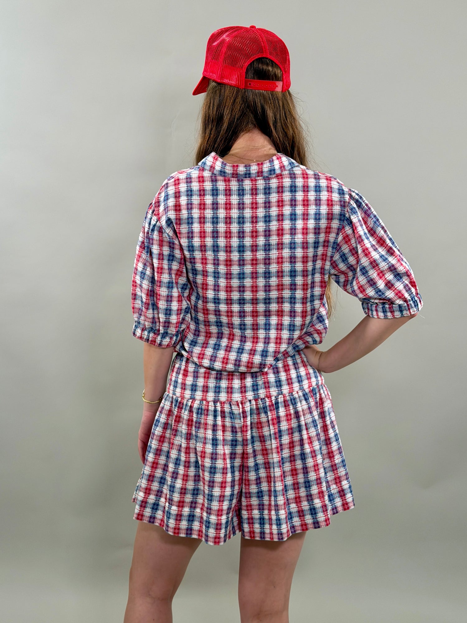 Person wearing a red, white, and blue checkered outfit with a red cap on a plain background