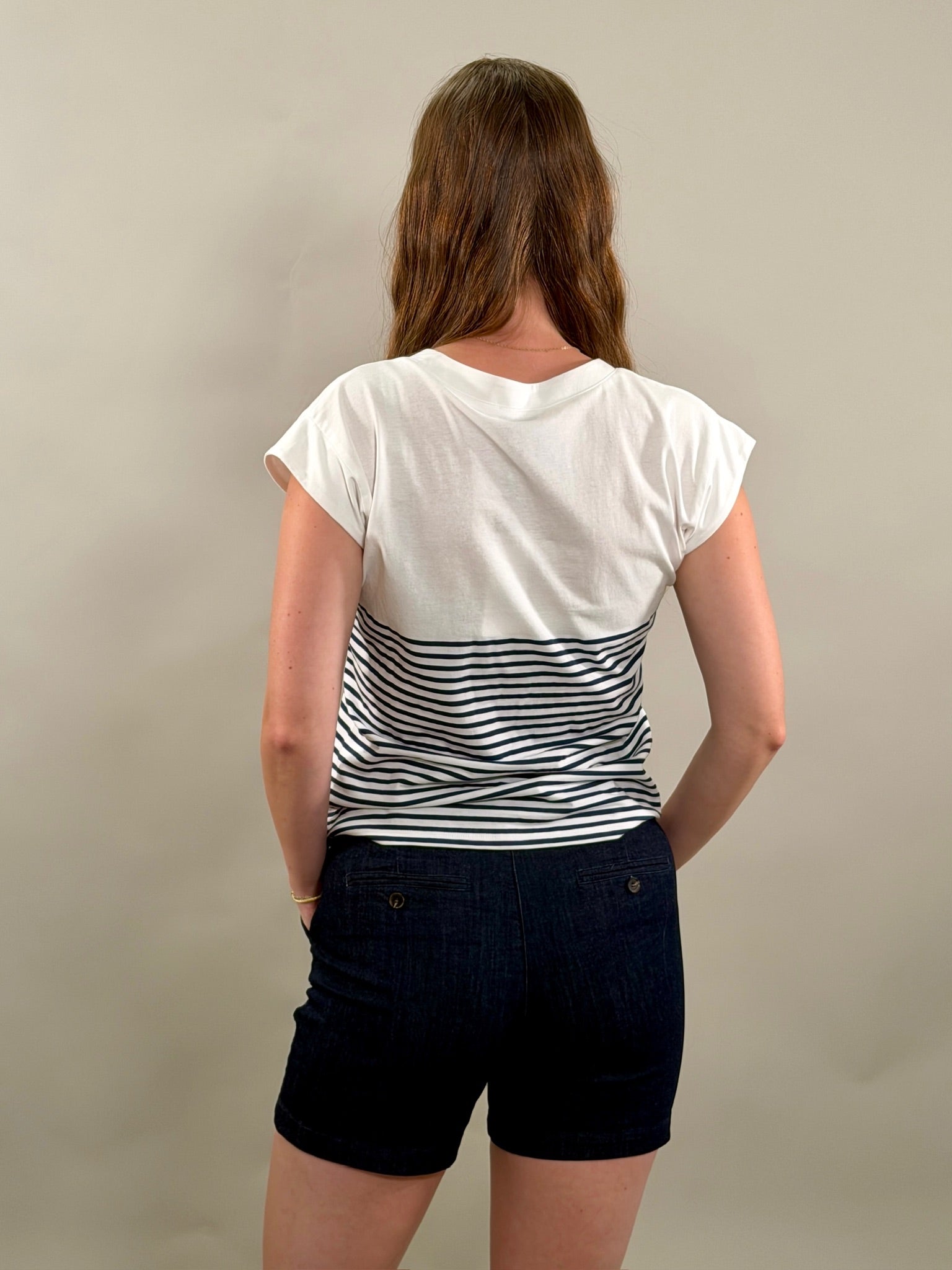 Rear view of a woman wearing a white t-shirt with a navy striped design and navy shorts on a plain background