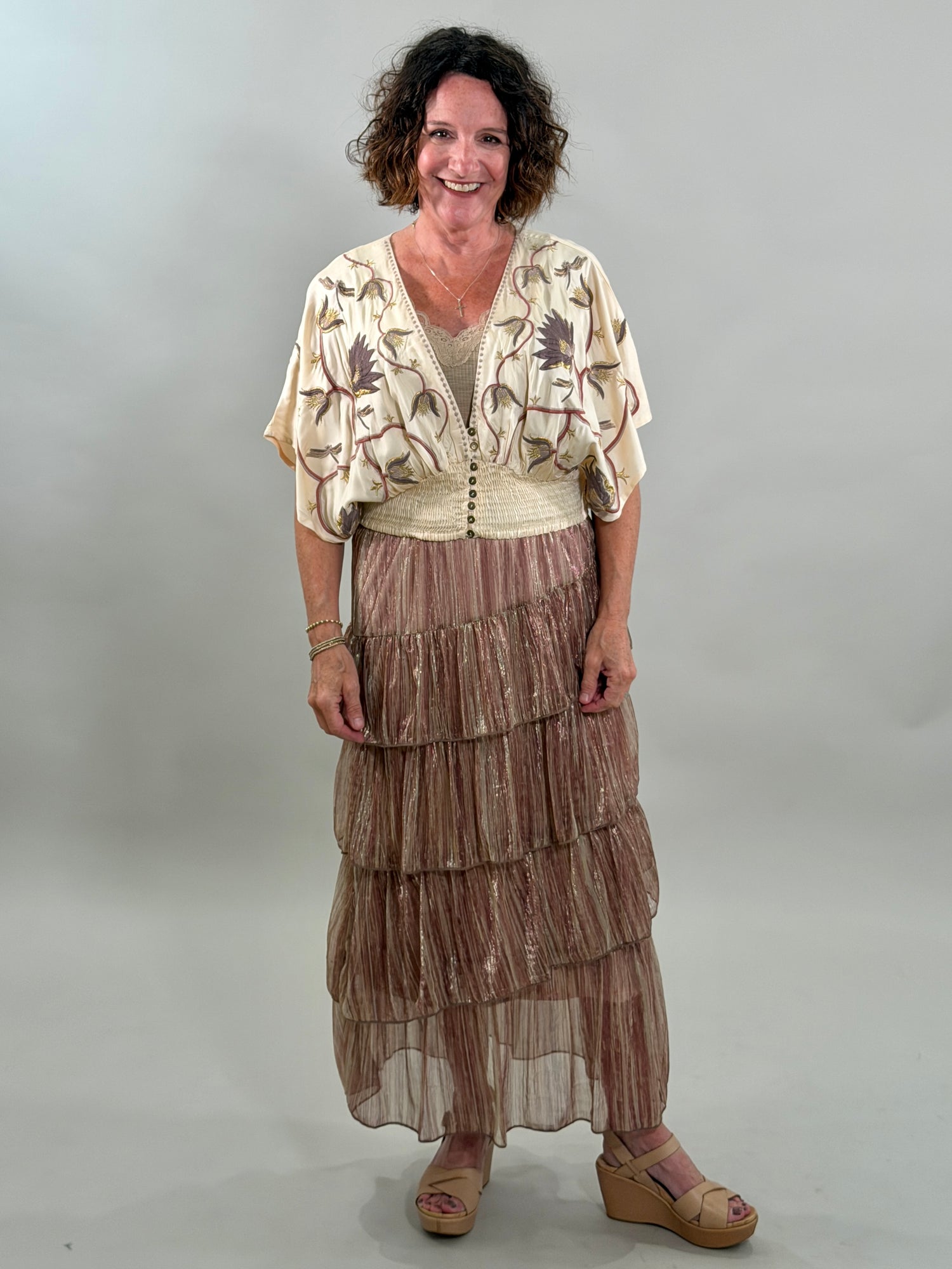Woman wearing a patterned top and tiered skirt against a plain background