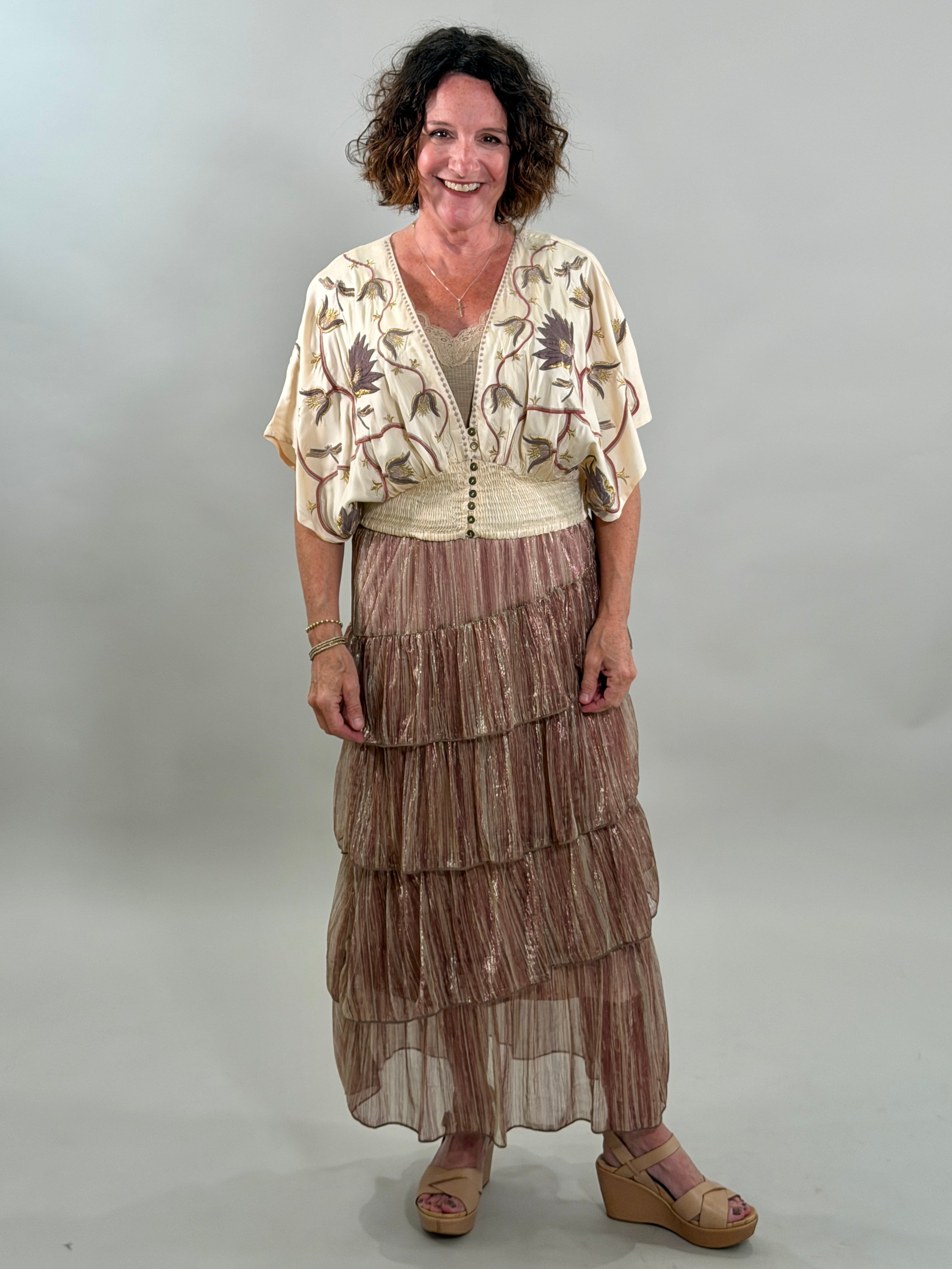 Woman wearing a patterned top and tiered skirt against a plain background