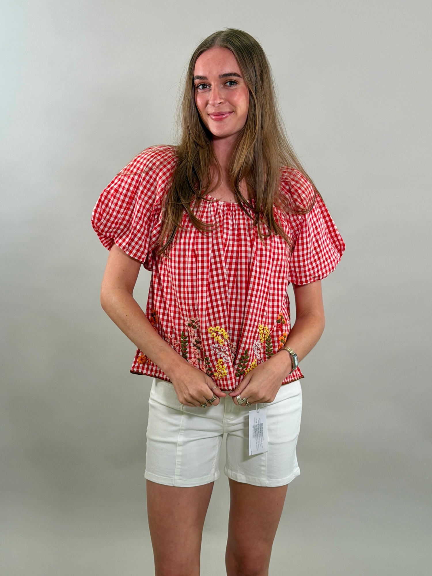 Woman wearing a red checkered blouse and white shorts against a plain background
