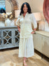 Full body view of a woman wearing a cream-colored 100% cotton button-down shirt with a tailored pintuck back waist detail with matching cream midi skirt.