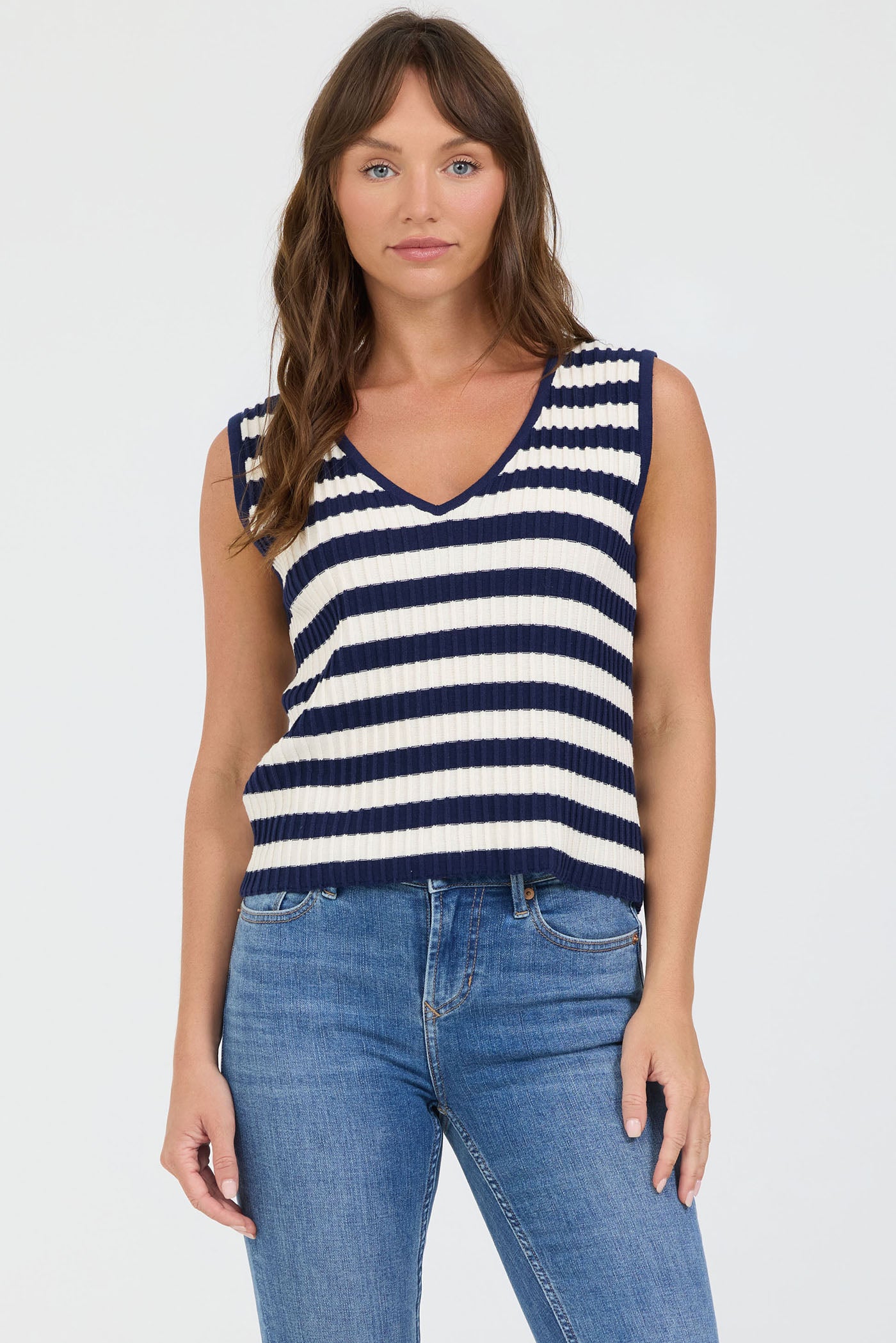 Woman wearing a navy and white striped sleeveless top with blue jeans on a white background