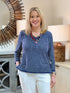 Close up of a blonde woman smiling while wearing a navy and white striped cotton-linen V-neck pullover top with white trousers and a colorful necklace.