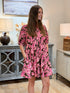 Woman wearing a pink and brown floral 100% cotton shirt dress with front pleats and pockets.