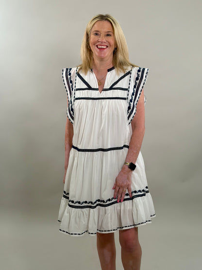 Woman wearing a white dress with navy trim against a plain background