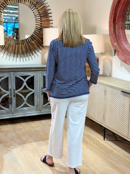 Rear full body view of a blonde woman wearing a navy and white striped cotton-linen V-neck pullover top with white trousers.