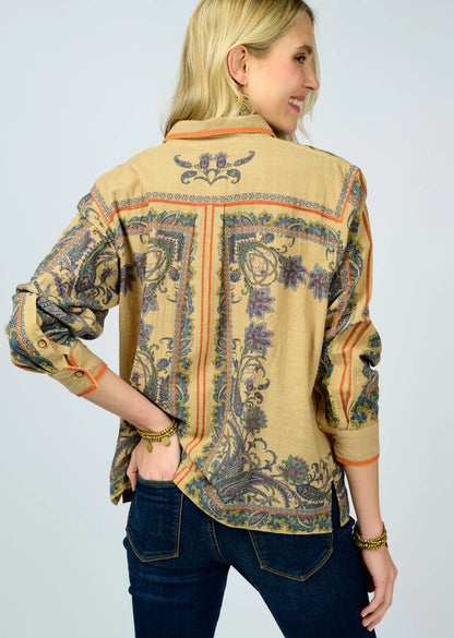 Woman wearing a patterned beige shirt with long sleeves on a plain background