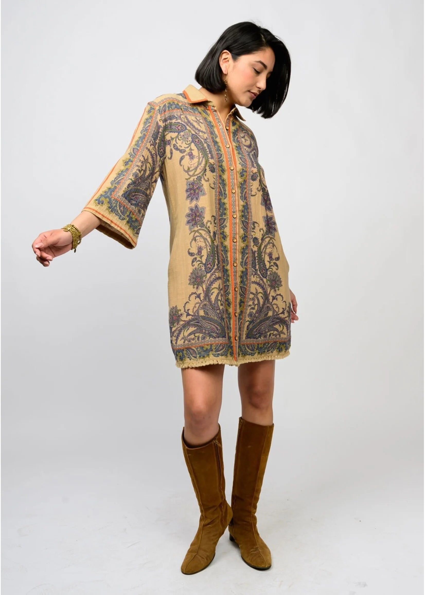 Woman wearing a patterned dress with bell sleeves and brown boots on a white background