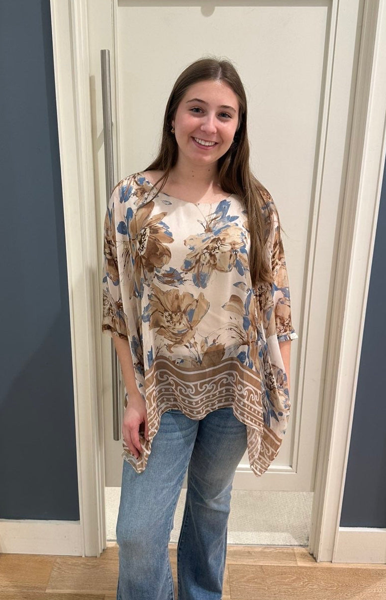Woman wearing a floral blouse and jeans standing in a room with a door.