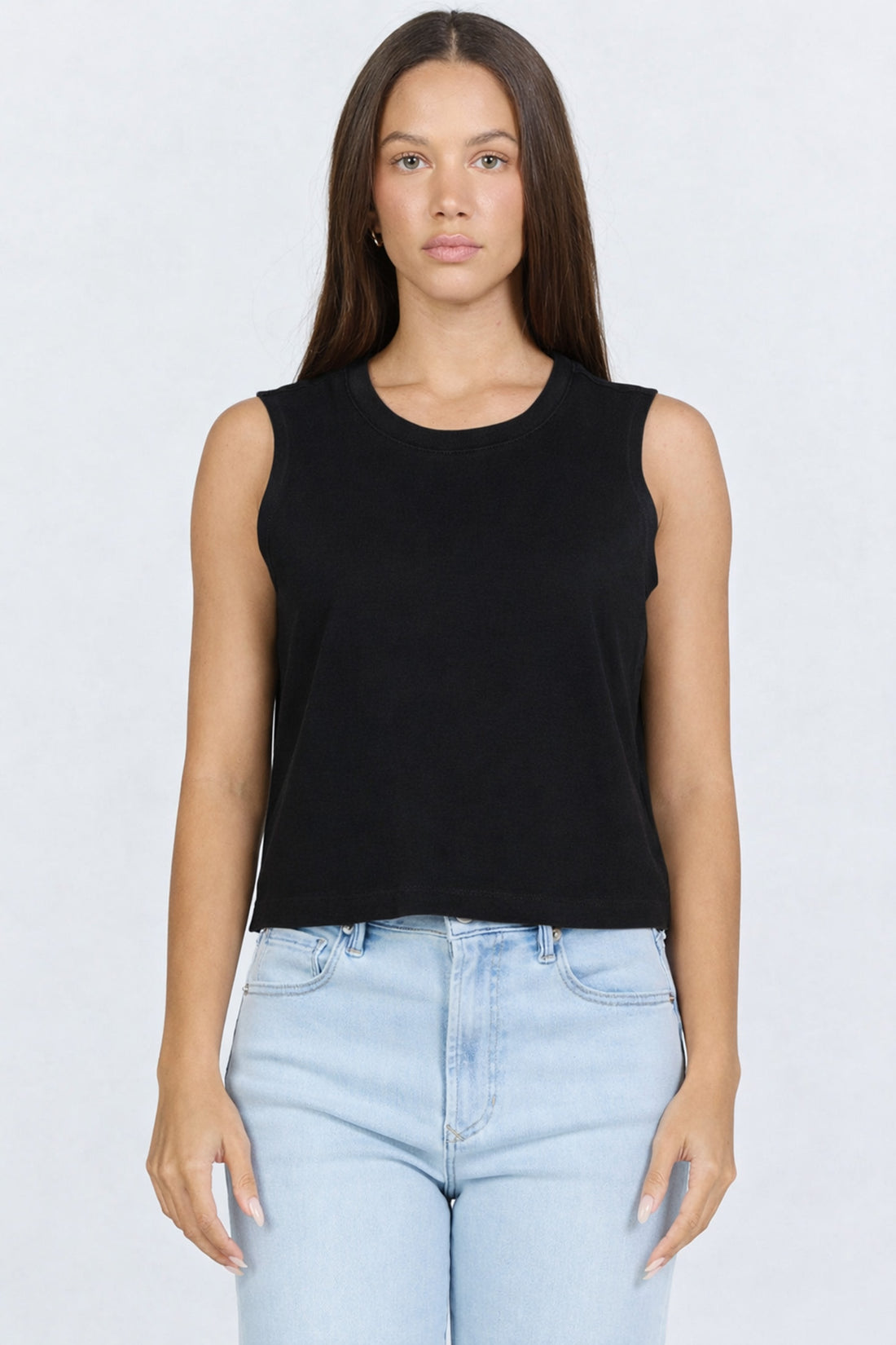 Front view of a woman wearing a black garment-dyed sleeveless crew neck cotton tank top with light blue jeans.