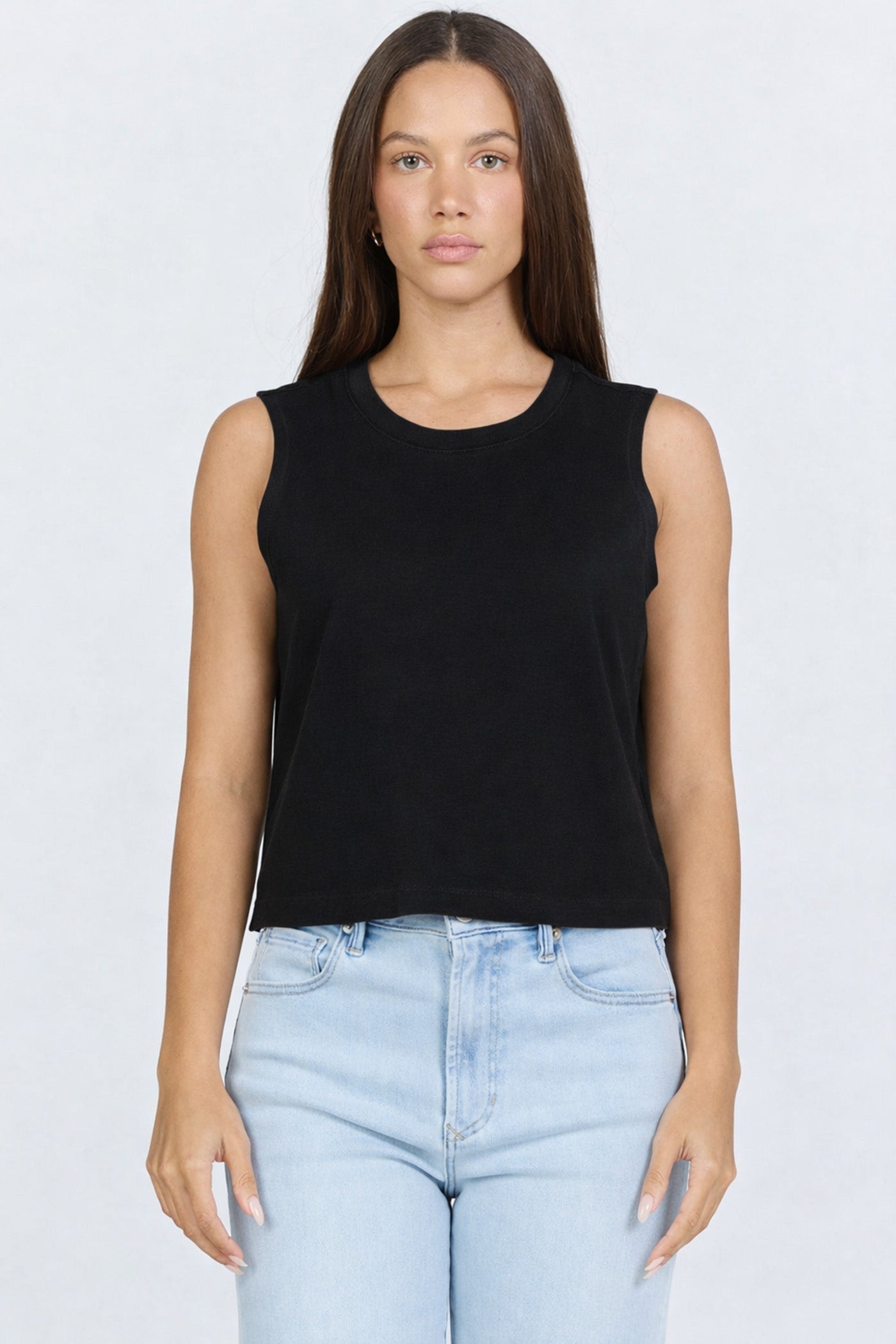 Front view of a woman wearing a black garment-dyed sleeveless crew neck cotton tank top with light blue jeans.