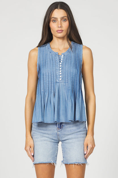 A woman wearing the sleeveless pleated Tencel tank top in denim blue with light-wash denim shorts