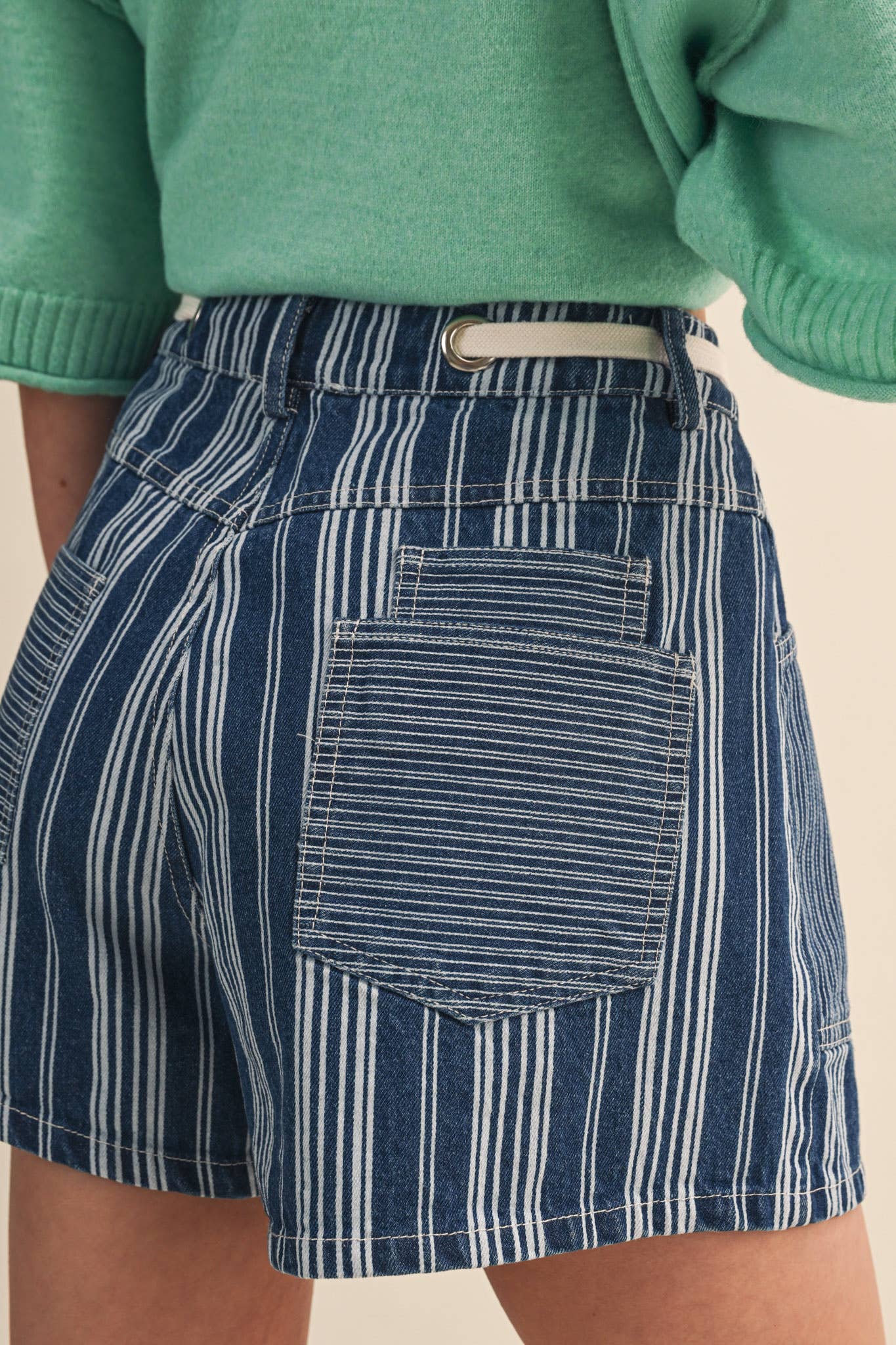 Close up of a rear view of navy and white striped skirt worn with a green sweater on a beige background