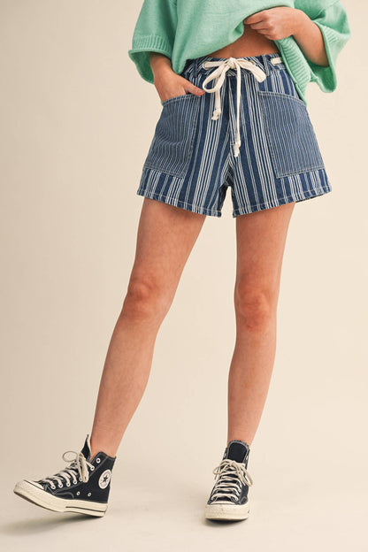 Person wearing blue striped shorts and black sneakers on a beige background
