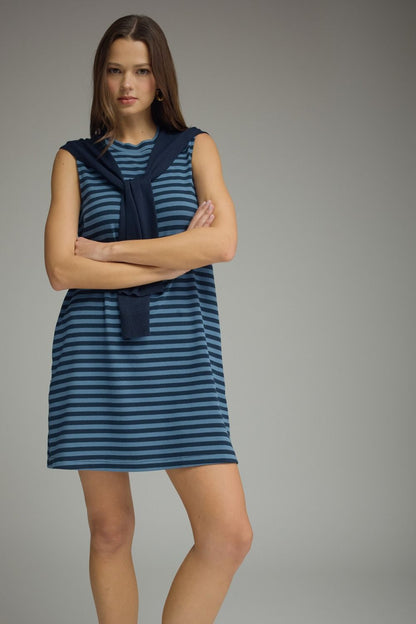 Model wearing a blue and navy striped sleeveless mini dress with a dark sweater accent tied around her shoulders.