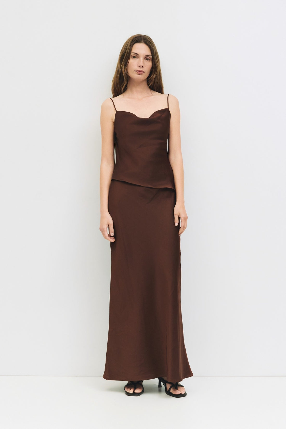 Full body view of a woman wearing a chocolate brown satin cowl neck tank.