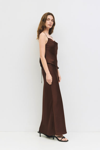 Full body side view of a woman wearing a chocolate brown satin cowl neck tank.