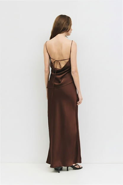 Rear view of a woman wearing a chocolate brown bias-cut satin midi skirt paired with black strappy sandals.