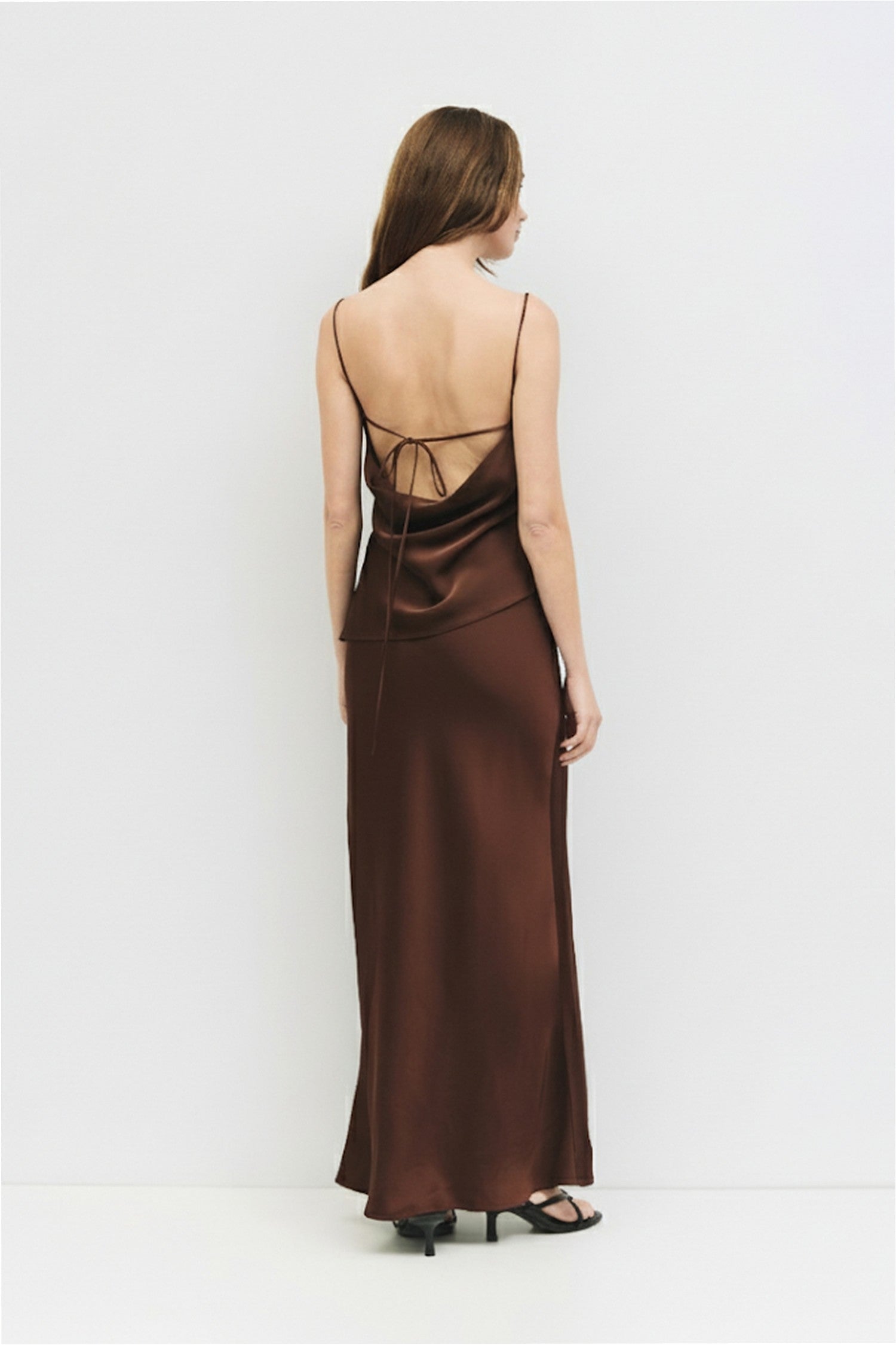 Rear full body view of a woman wearing a chocolate brown satin cowl neck tank.