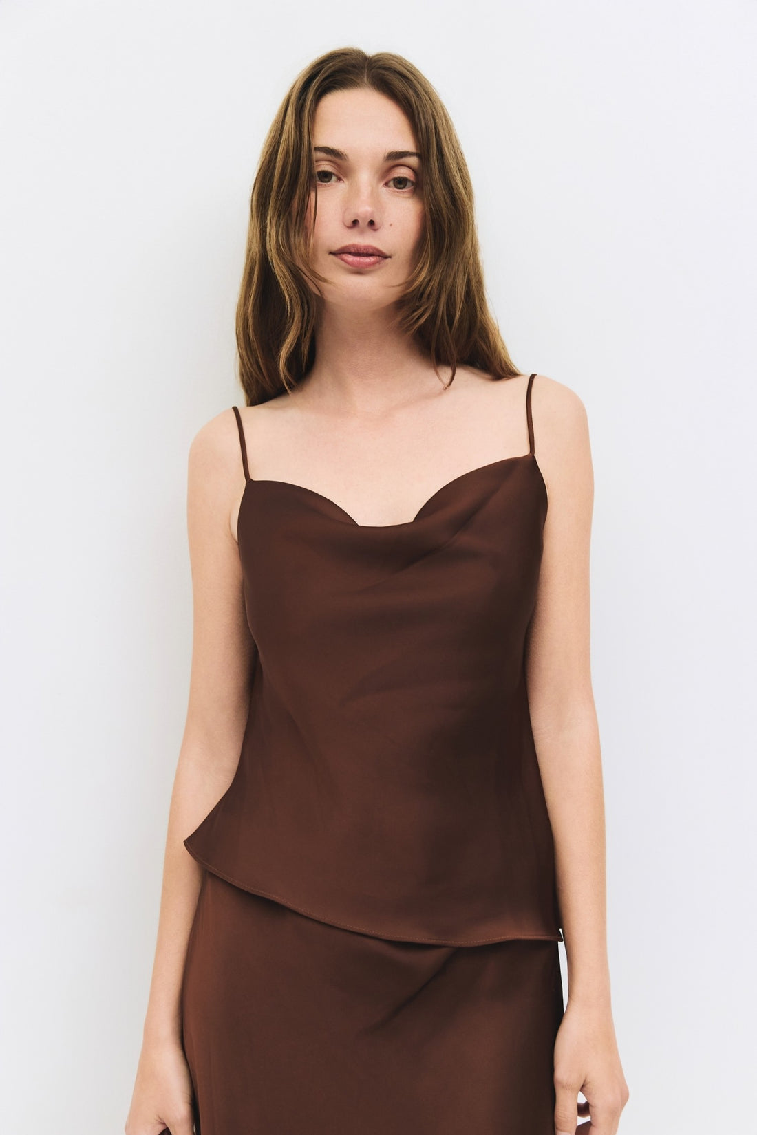 Close up view of a woman wearing a chocolate brown satin cowl neck tank.