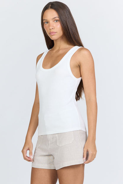 Side view of a woman wearing a fitted white scoop-neck ribbed racerback tank top with beige linen shorts.