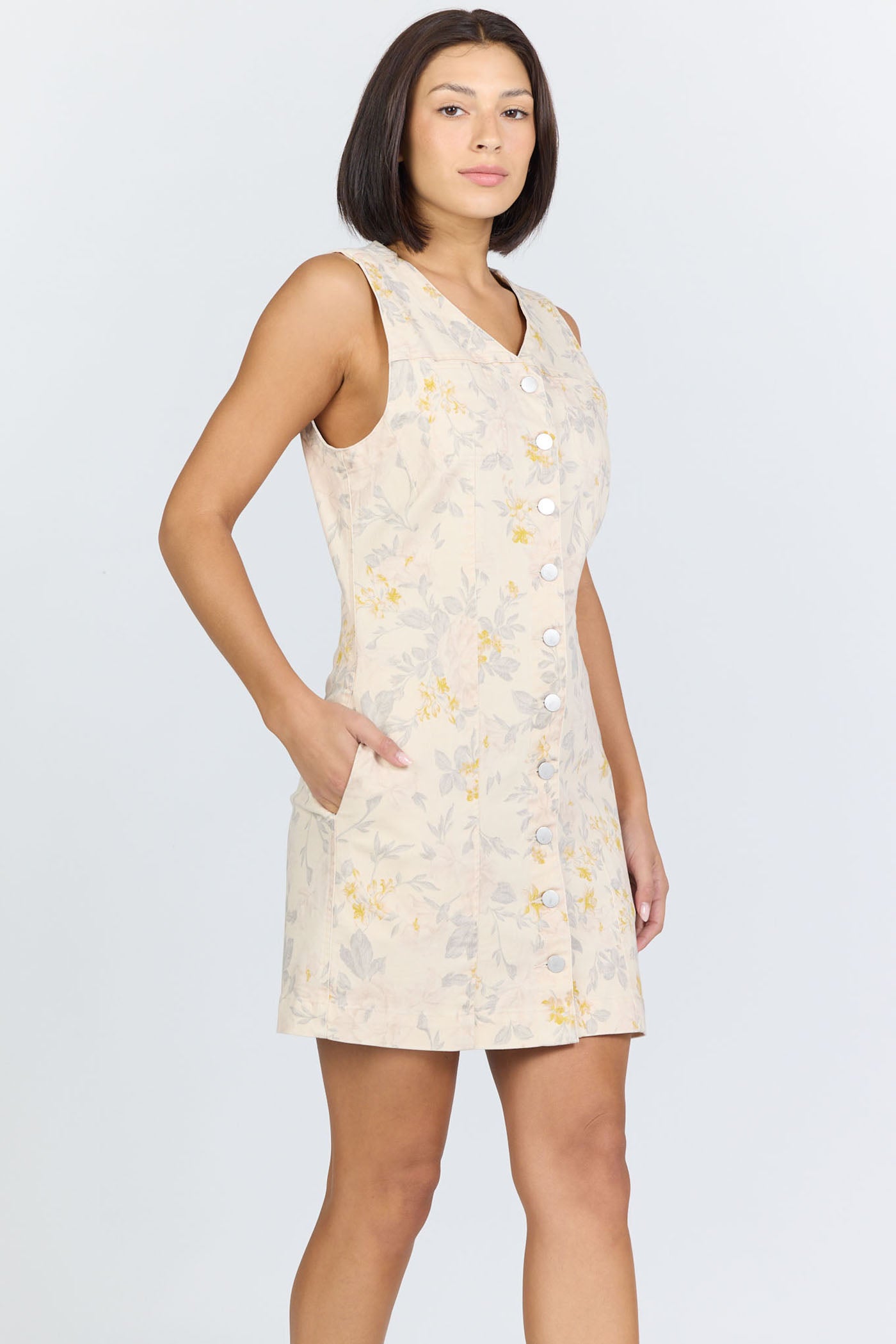 Side view of a model with short dark hair wearing a cream floral button-front sleeveless dress.