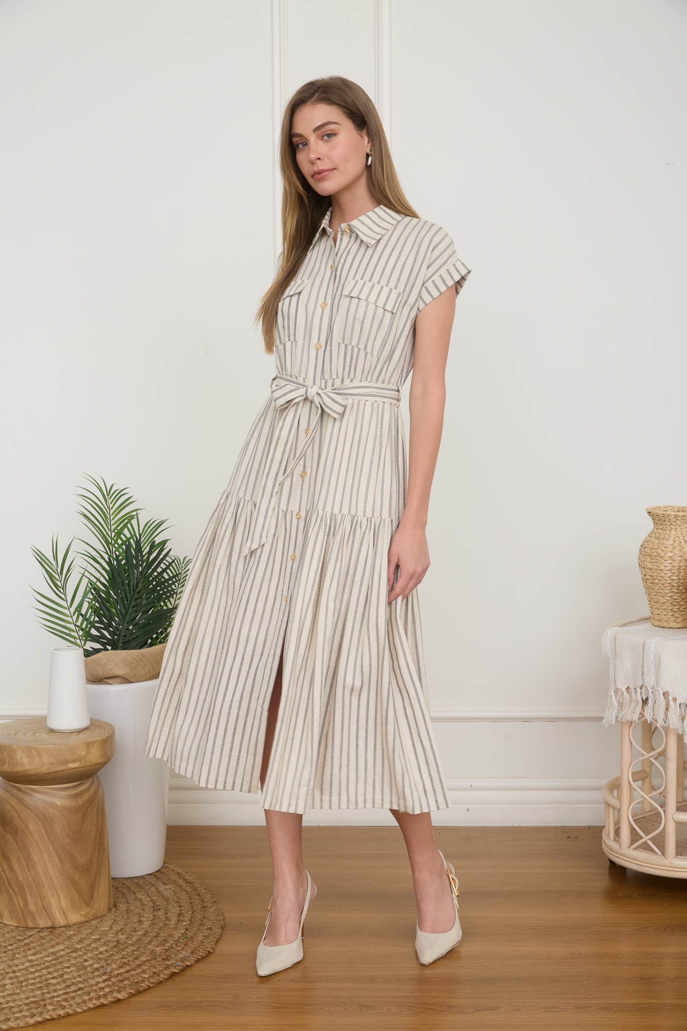 Woman wearing a light taupe and cream vertically striped midi shirt dress with a tie belt, short cap sleeves, and high heels.