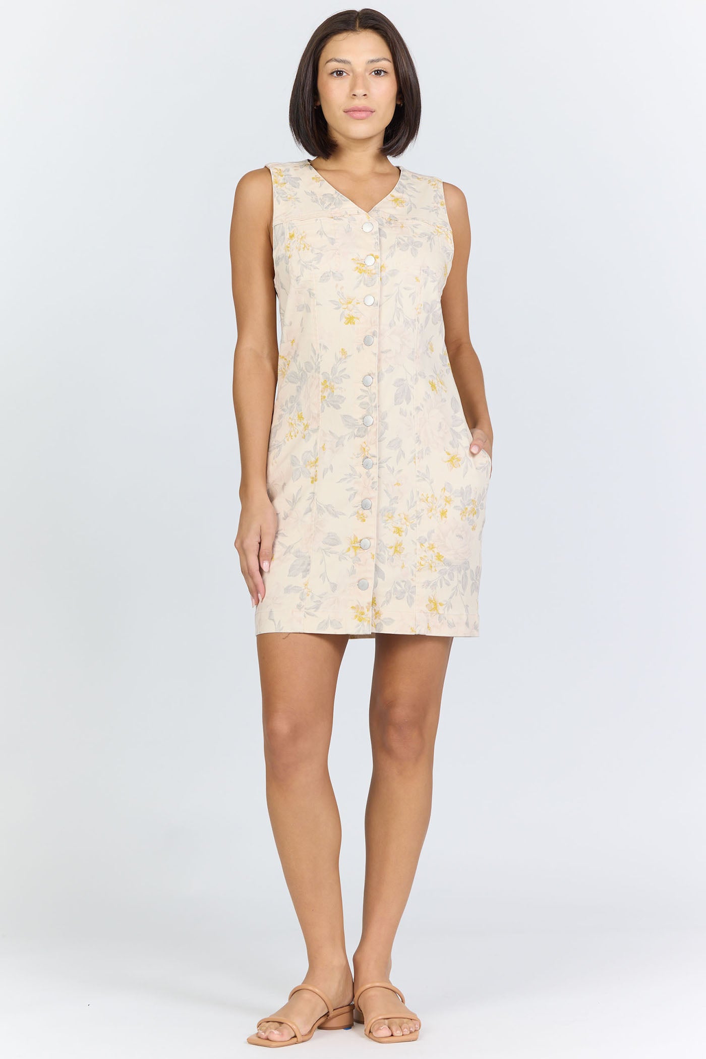 Full body view of a model with short dark hair wearing a cream floral button-front sleeveless dress.
